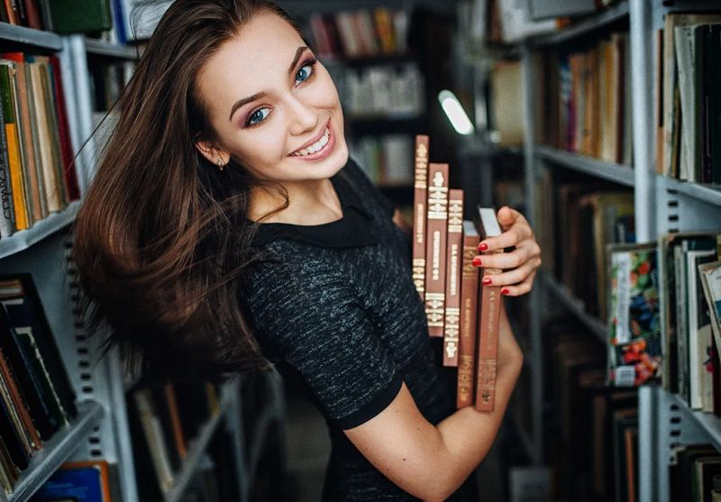 Девушка со стопкой книг в библиотеке