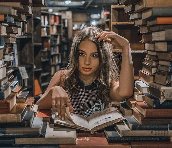 Девушка сидит среди стопки книг