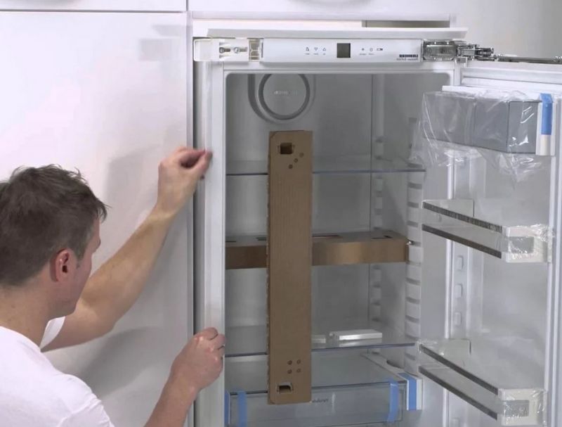 Рабочий устанавливает встроенный холодильник